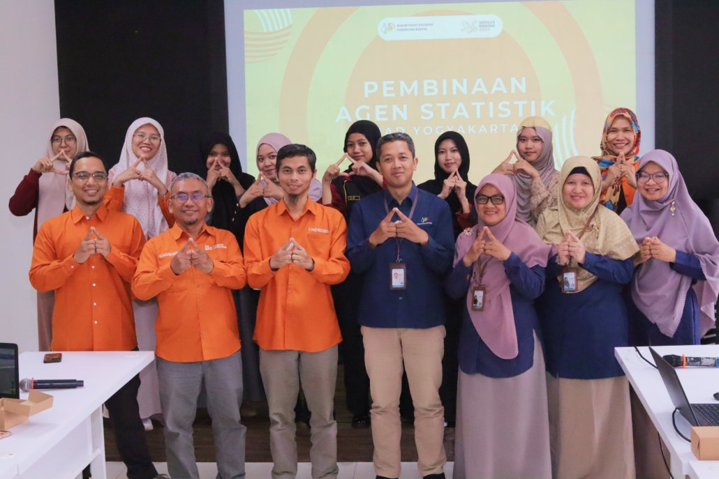 Foto bersama narasumber dari BPS, dosen FAST UAD, dan mahasiswa peserta Pembinaan Agen Statistik Tahap V di Universitas Ahmad Dahlan Yogyakarta. Peserta berpose dengan simbol tangan segitiga di depan layar proyektor.