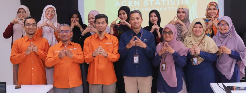 Foto bersama narasumber dari BPS, dosen FAST UAD, dan mahasiswa peserta Pembinaan Agen Statistik Tahap V di Universitas Ahmad Dahlan Yogyakarta. Peserta berpose dengan simbol tangan segitiga di depan layar proyektor.
